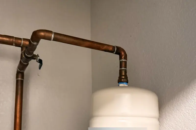 Small white thermal expansion tank hanging from a copper cold-water line