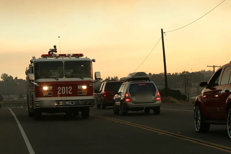 Fire engine with its lights on driving under a smoky sunset sky during the 2007 San Diego County wildfires