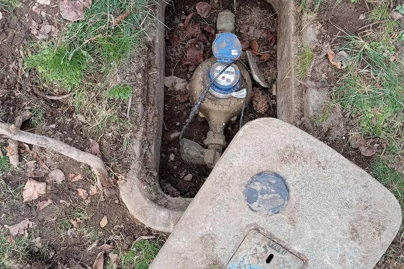 Open in-ground meter box with the lid lifted, showing the water meter used for a no-flow leak check
