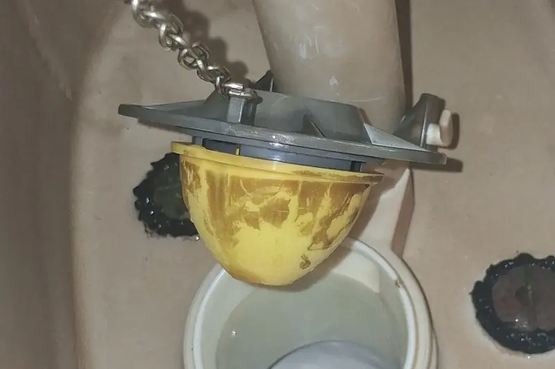 Inside a drained toilet tank: the rubber flapper lifted off the flush valve seat on its chain