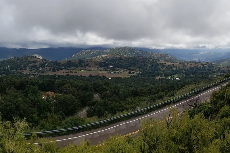 View from a mountain road down over a valley of groves, ranches and rolling hills below Palomar Mountain on a cloudy day